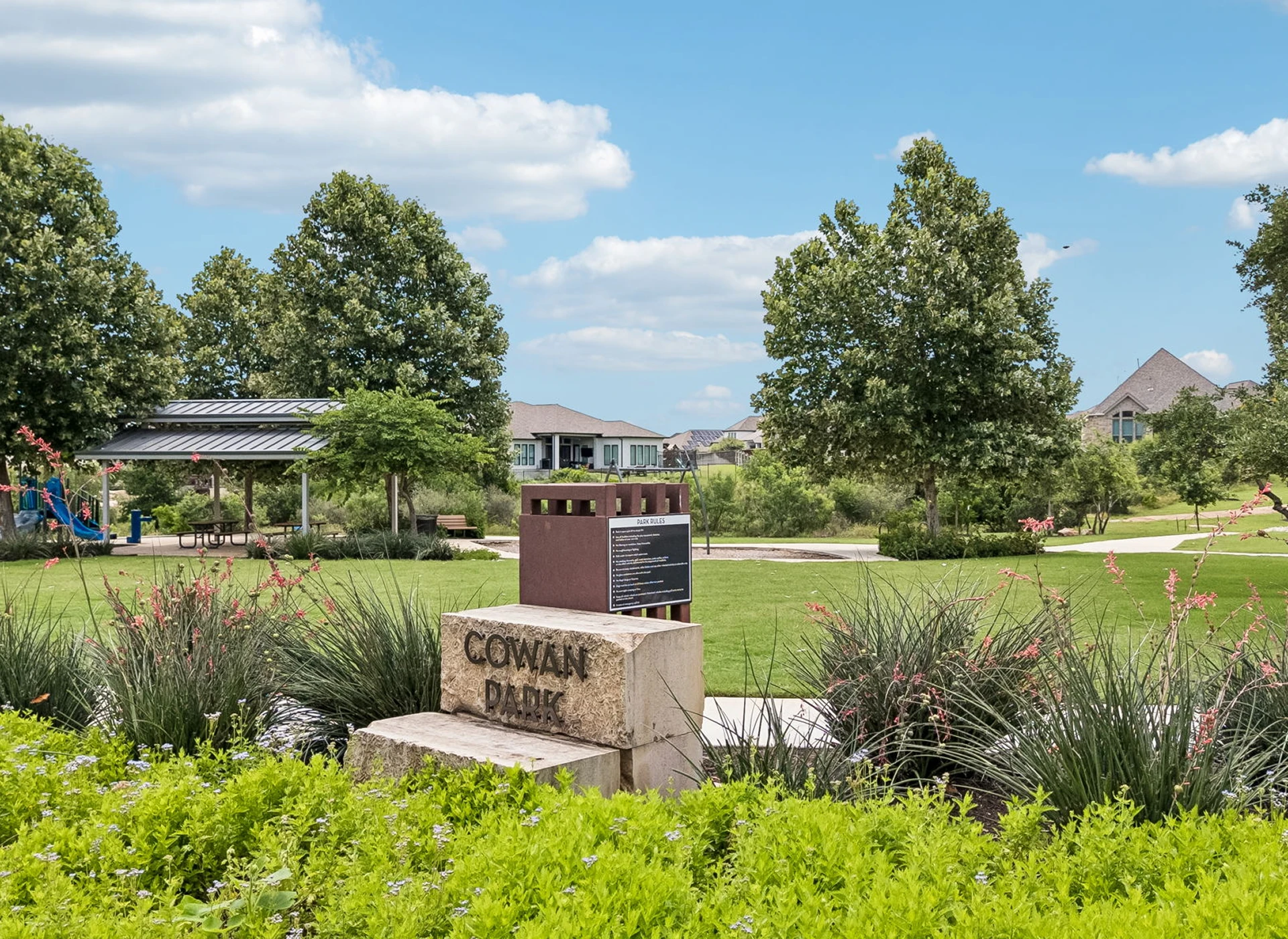Cowan Park sign amidst green park scenery.